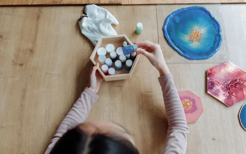 Top view of a woman creating vibrant resin art on wooden surface at home.