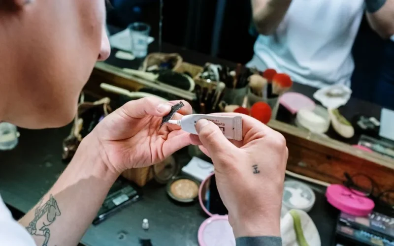 Close-up of hands applying false eyelashes with glue in a makeup room.