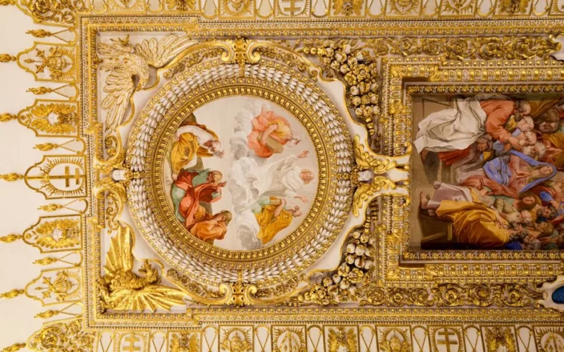 Ornate Baroque ceiling with detailed frescoes and gold accents depicting classical art.