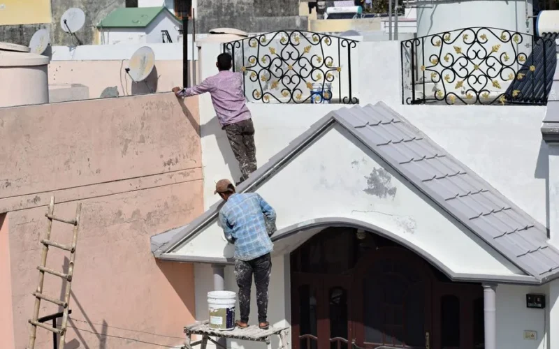 Two workers engaged in painting and renovating a building roof, showcasing a construction scene.