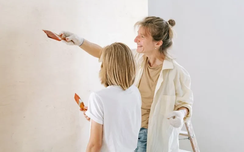 A smiling mother and child collaborate on painting a wall, showcasing a family home project.