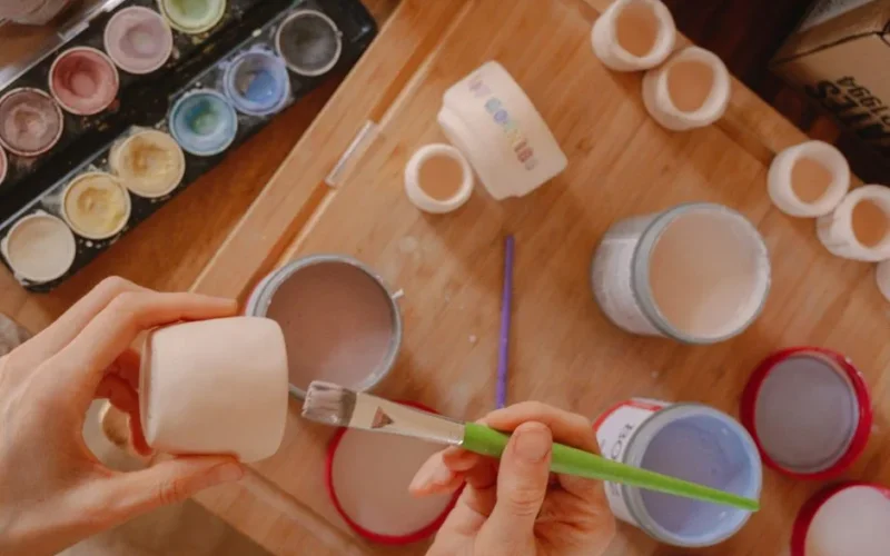 Hands painting ceramic pots with a variety of pastel colors, showcasing a creative art workshop.