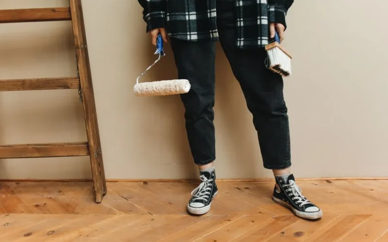 A person holding a paint roller and brush during a home renovation project.