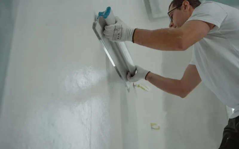 A man works on home renovation, applying plaster to an interior wall for a smooth finish.