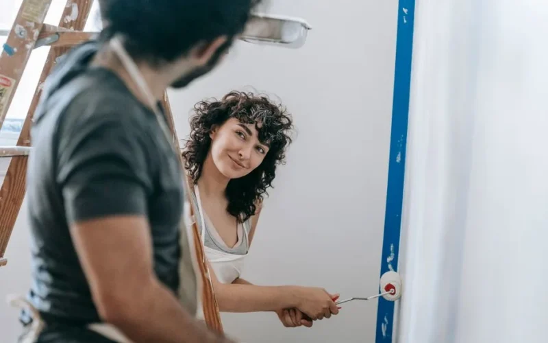 A happy couple painting walls together in their home, enjoying a playful moment during renovation.