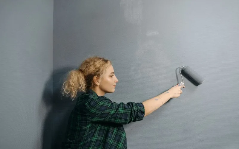 Young woman uses a paint roller to apply grey paint on an indoor wall, renovating her space.