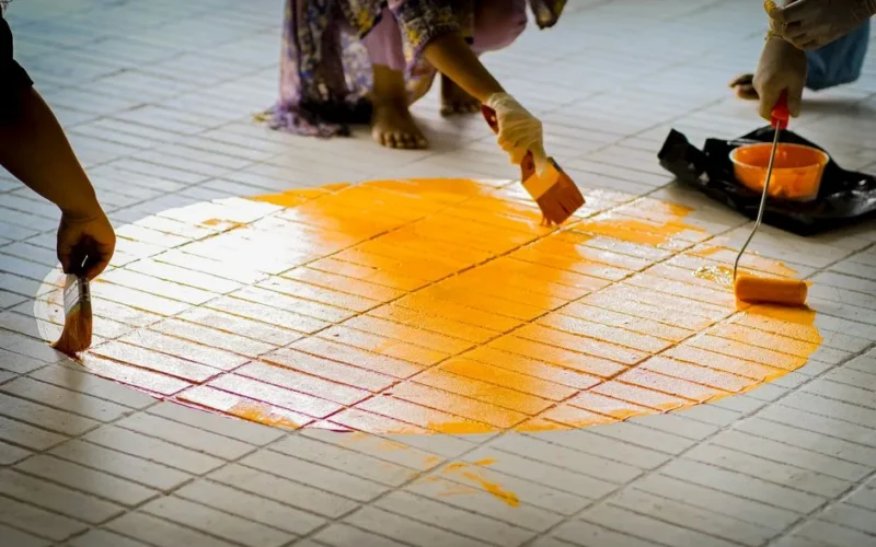 Group of people painting a vibrant orange circle on a tiled floor.