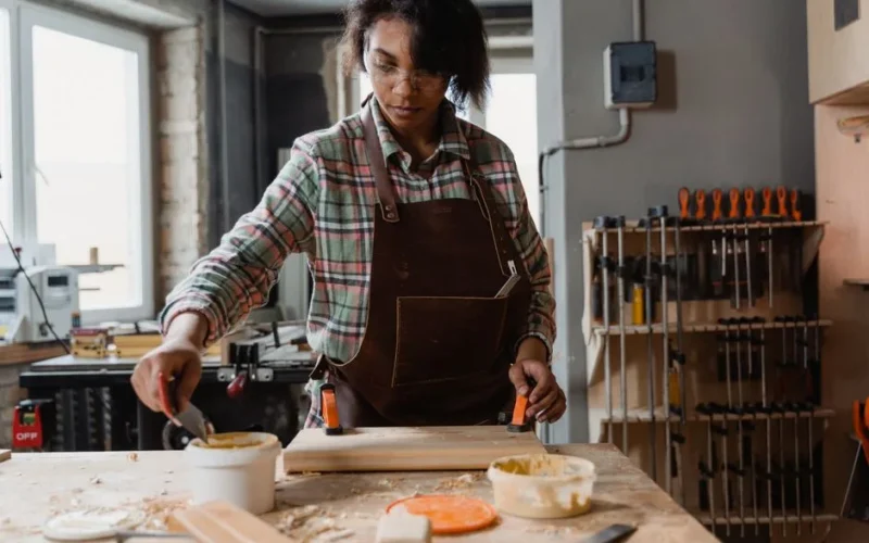 African American woman woodworking, applying glue in workshop setting. Focus on craftsmanship and woodworking tools.