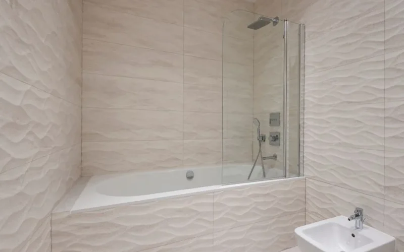 A sleek modern bathroom featuring a bathtub, shower, and beige textured tiles.