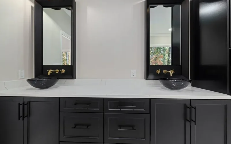 Elegant bathroom featuring black cabinets, vessel sinks, and gold hardware.