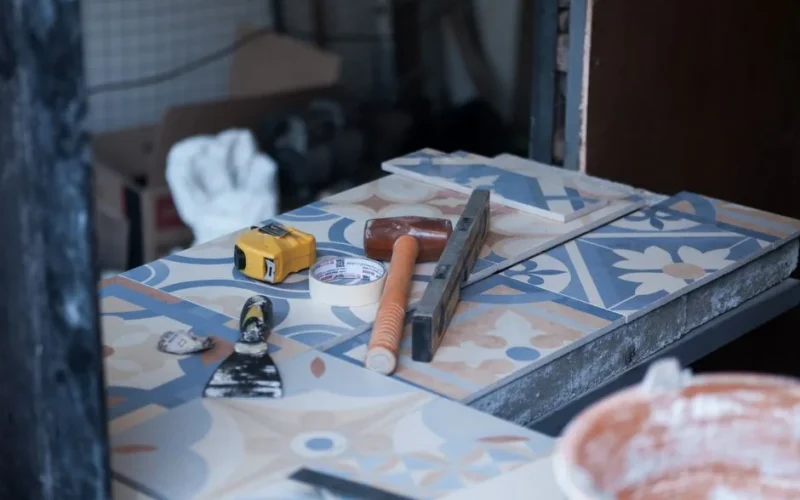 Tools and tiles on a construction site, ready for tiling work. Includes trowel, tape measure, and adhesive tape.