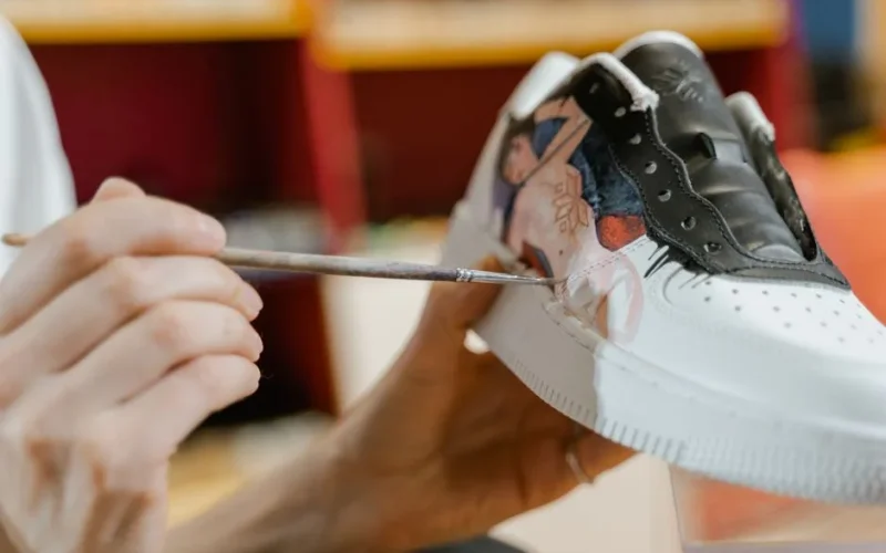 Close-up of hand painting a custom design on a white sneaker with a brush.