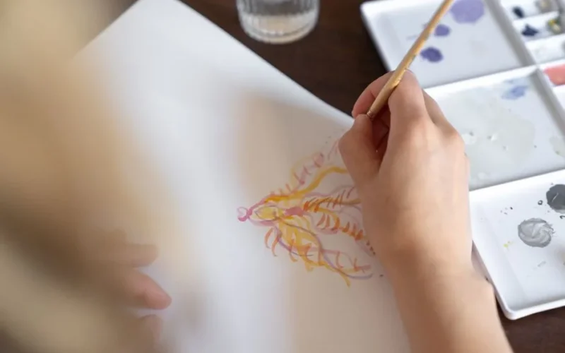 Close-up of a hand painting with watercolors, creating intricate designs on paper.