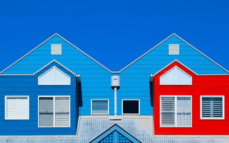 Brightly painted house facades in blue and red create a striking contrast against a clear blue sky.