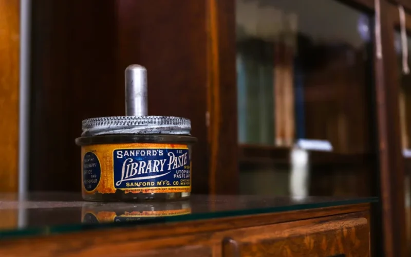 Close-up of a vintage Sanford library paste jar on a wooden bookshelf.