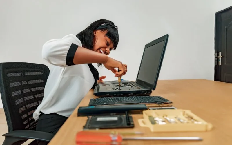 Woman repairing a laptop at a desk with tools, showcasing technology and skill.