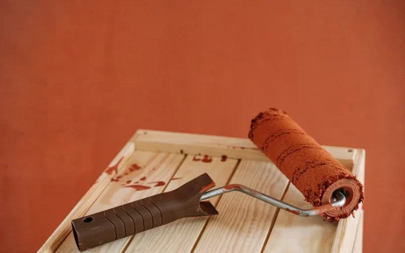 A paint roller with rustic brown paint on a wooden surface against an earthy wall.