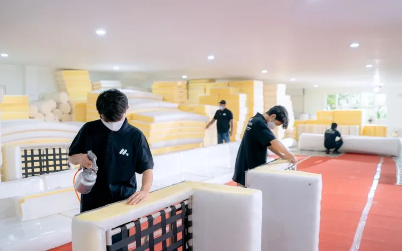 Employees crafting furniture in a workshop, focusing on cushion assembly and quality control.