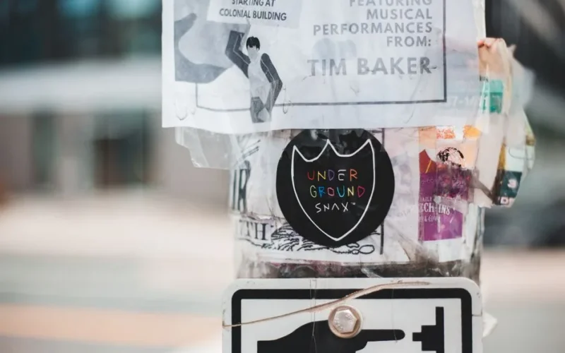 Metal street pole covered with different stickers and ads placed on street in daytime