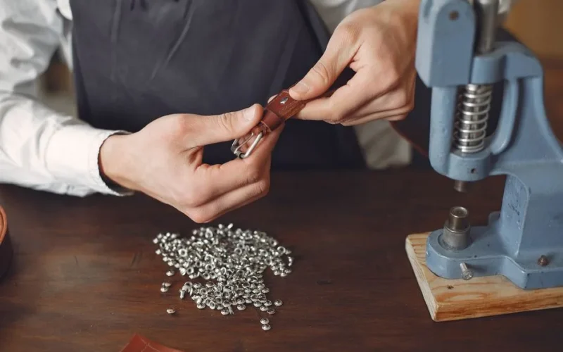 From above of anonymous artisan using rivet press and setting rivets on leather belt while working at table in contemporary workshop