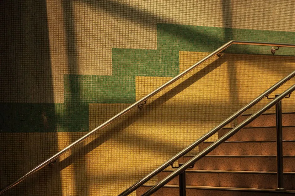 Sunlight casts shadows on a mosaic tiled staircase with a metal handrail in Ankara.