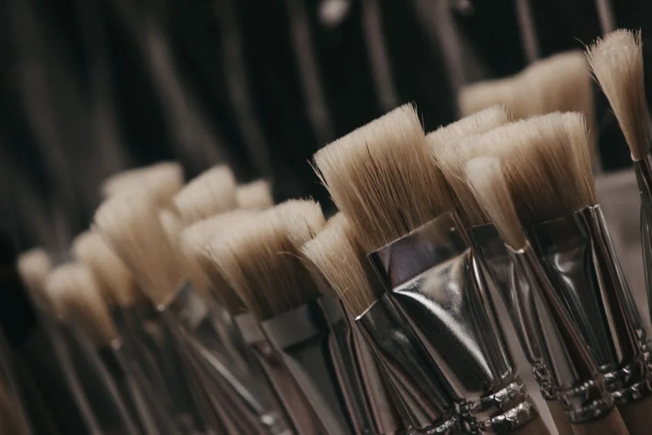 A detailed close-up shot of artist paint brushes featuring soft white bristles and metallic handles.