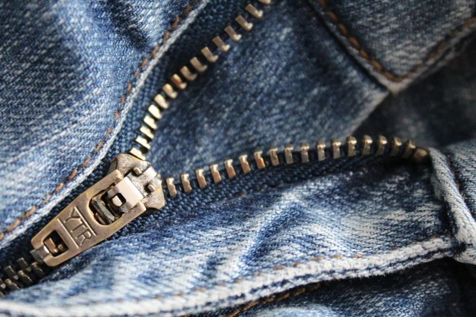 Detailed shot of a metal zipper on blue denim fabric, showcasing texture and craftsmanship.