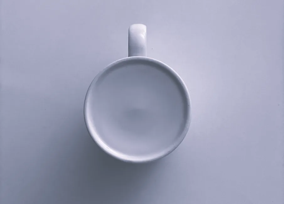 A simple, elegant top-down view of an empty white coffee mug on a white surface.