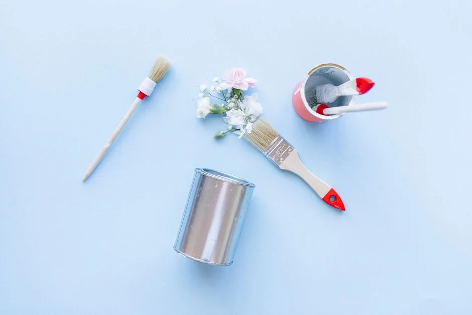 Creative top view of paintbrushes, cans, and flowers against a light blue background.