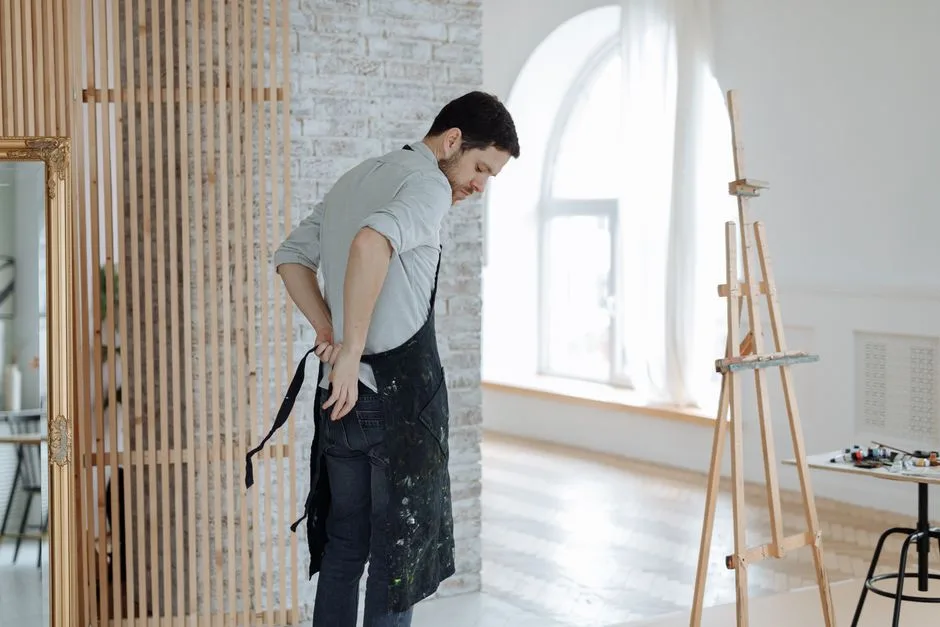 Creative man putting on apron in a bright studio with art supplies and easel, preparing to paint.
