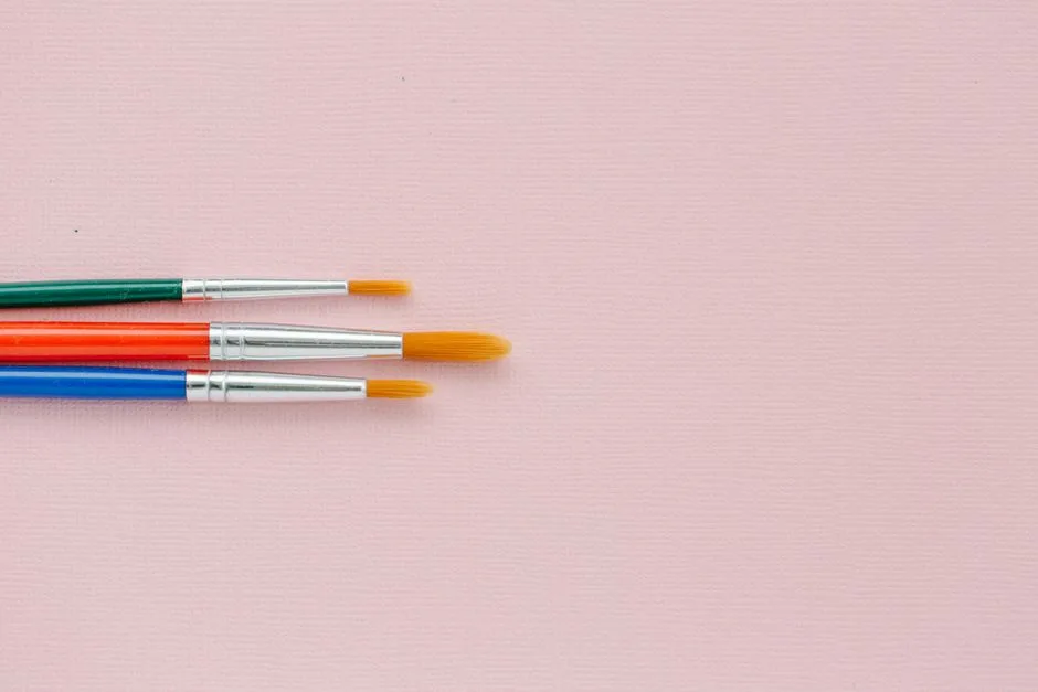 Three vibrant paintbrushes on a pink canvas providing ample copy space.