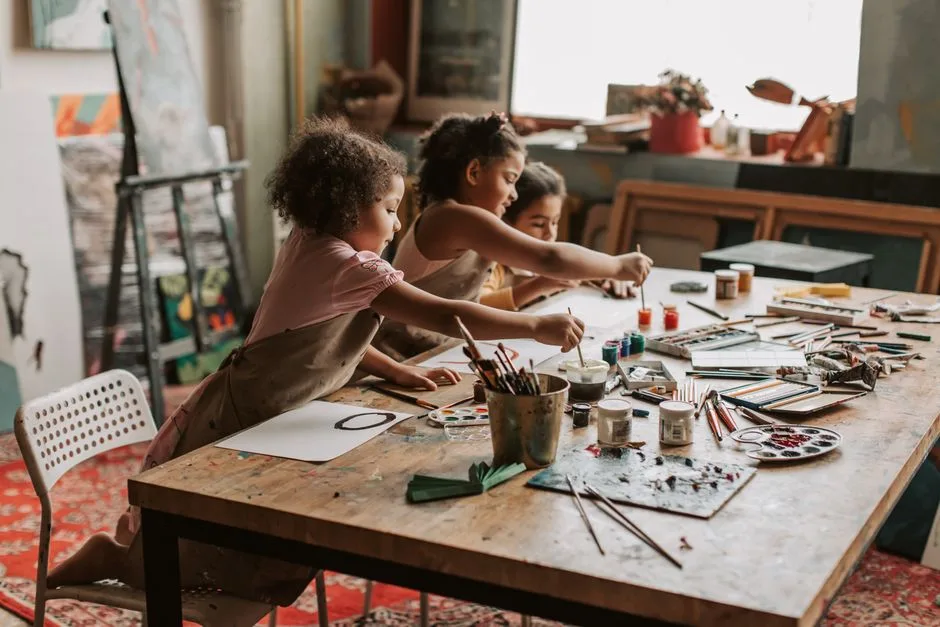 Three young girls engaged in painting at an indoor art studio, exploring their creativity.