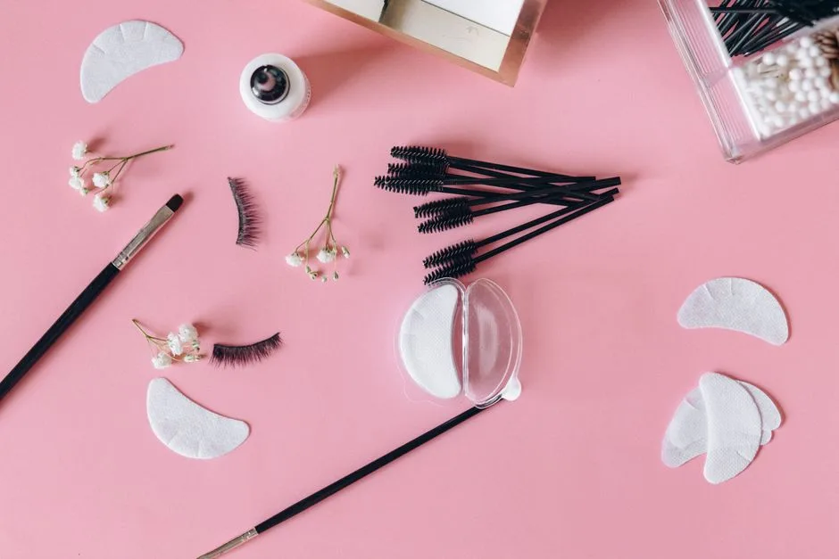 Aesthetic makeup tools and beauty items arranged on a pink surface.