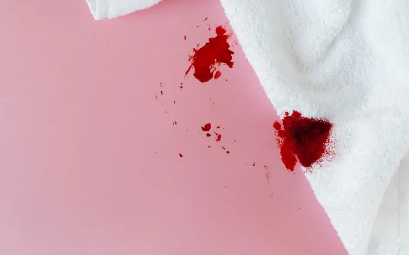 White towel with red blood stains on pink surface, showing menstrual concept.
