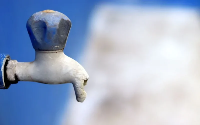 Detailed image of a broken faucet against a blurred blue background, emphasizing neglect.
