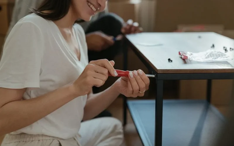 Woman smiling while assembling a table using a screwdriver in a home setting.