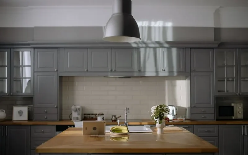 A sleek kitchen with gray cabinets, wooden countertops, and modern lighting.