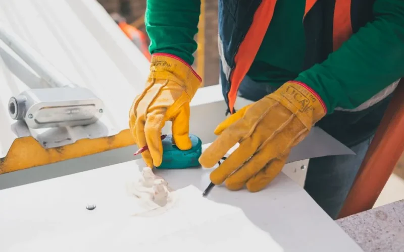 Electrician measuring on rooftop, wearing protective gloves, during daylight.