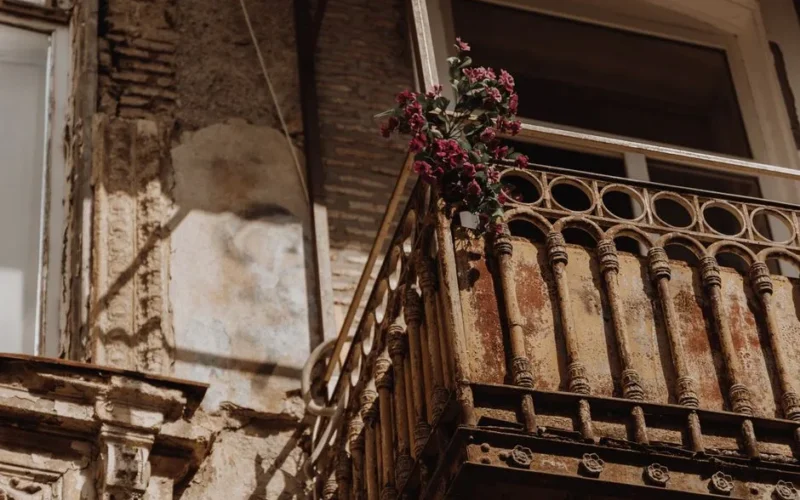 A rustic balcony with vibrant flowers in sunlight, highlighting weathered textures.