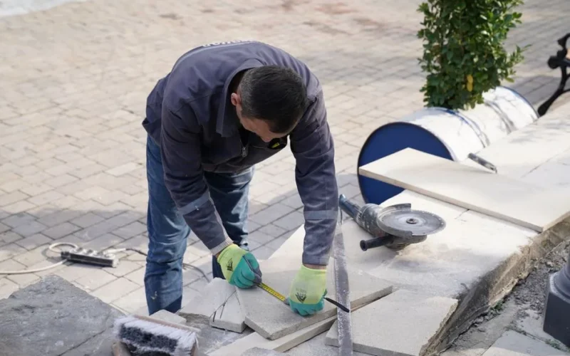 A construction worker measuring tiles outdoors with precision tools.