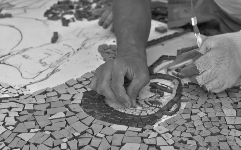 Close-up of hands meticulously crafting a mosaic, showcasing intricate artistry and craftsmanship.