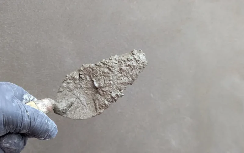 Hand wearing glove holds plaster trowel against smooth wall, depicting construction work.