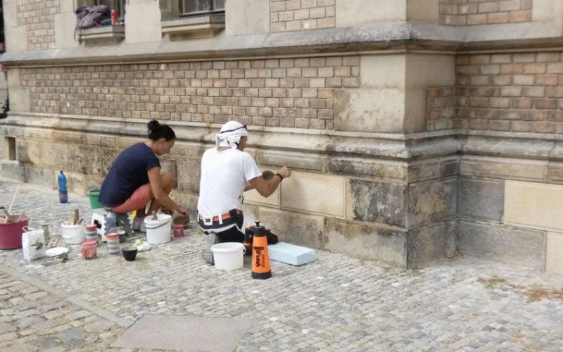 Two people engaged in restoring a historic brick building with tools and supplies.