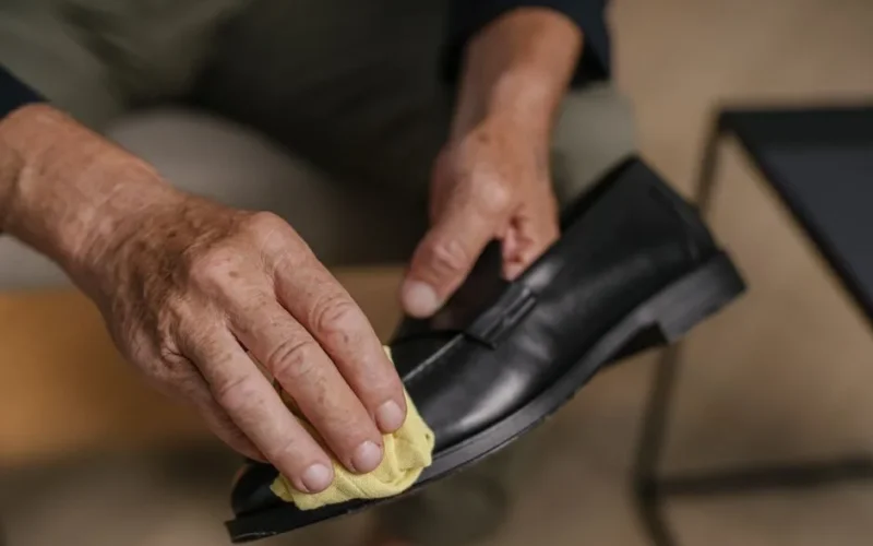 Detailed image of hands polishing a black leather shoe with a yellow cloth, emphasizing care and maintenance.
