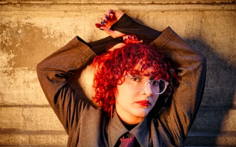 Fashionable woman with vibrant red curls posing confidently outdoors.