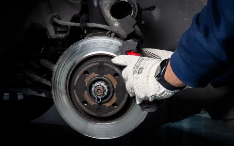 Mechanic working on car brake system in a workshop setting.