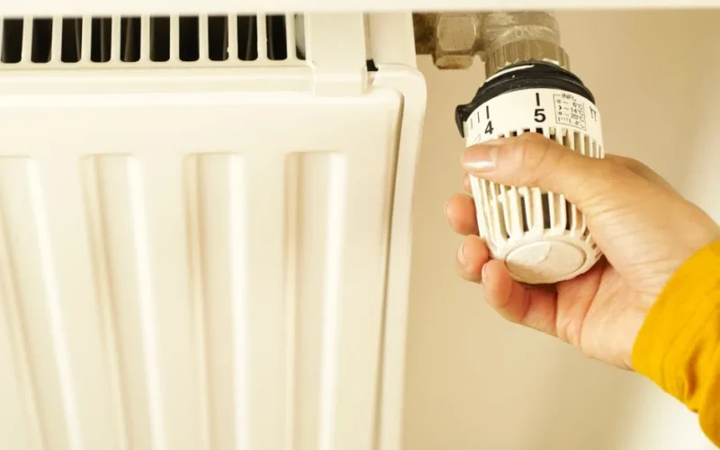 Close-up of hand adjusting radiator thermostat to control home heating temperature.