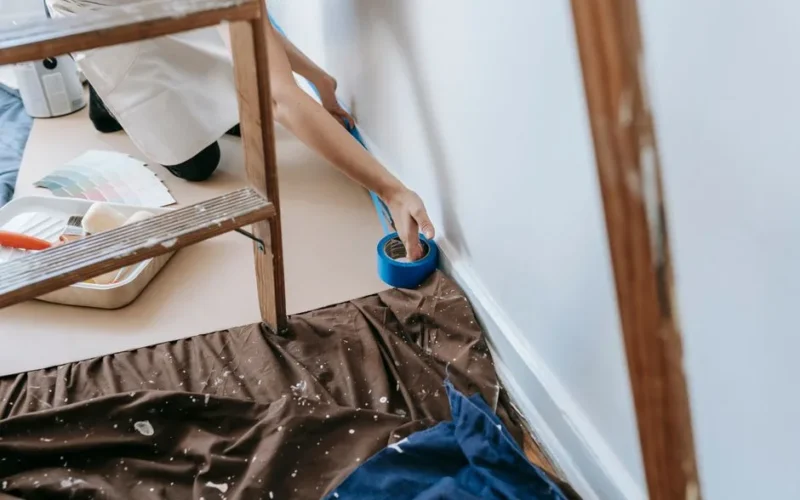 Woman preparing room for painting with adhesive tape and tools; home renovation project.