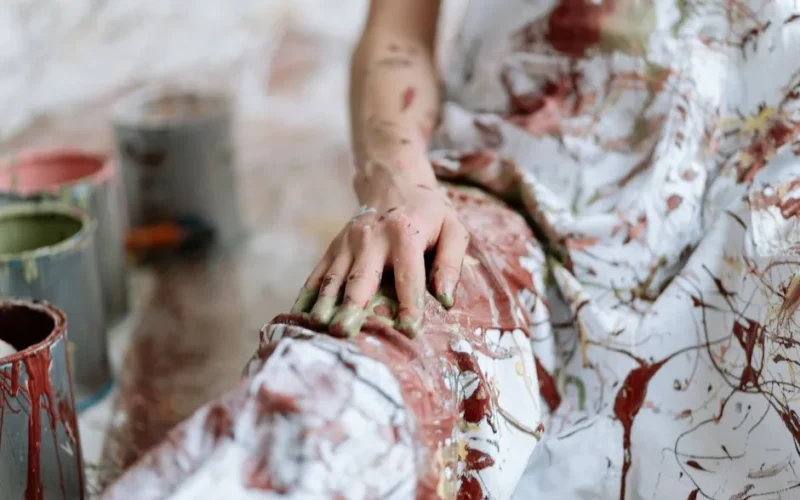 Close-up of a painted hand on a canvas, surrounded by colorful paint buckets.