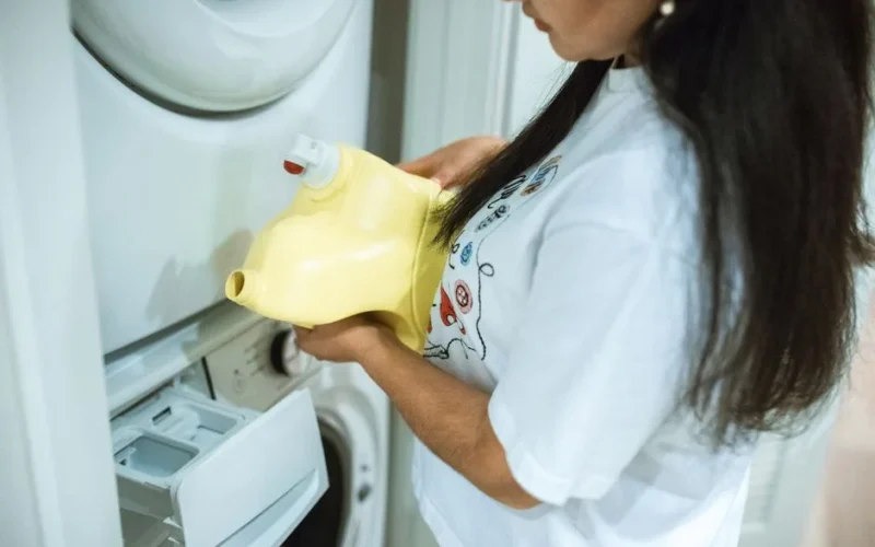 A woman pours detergent into a washing machine for a laundry cycle.
